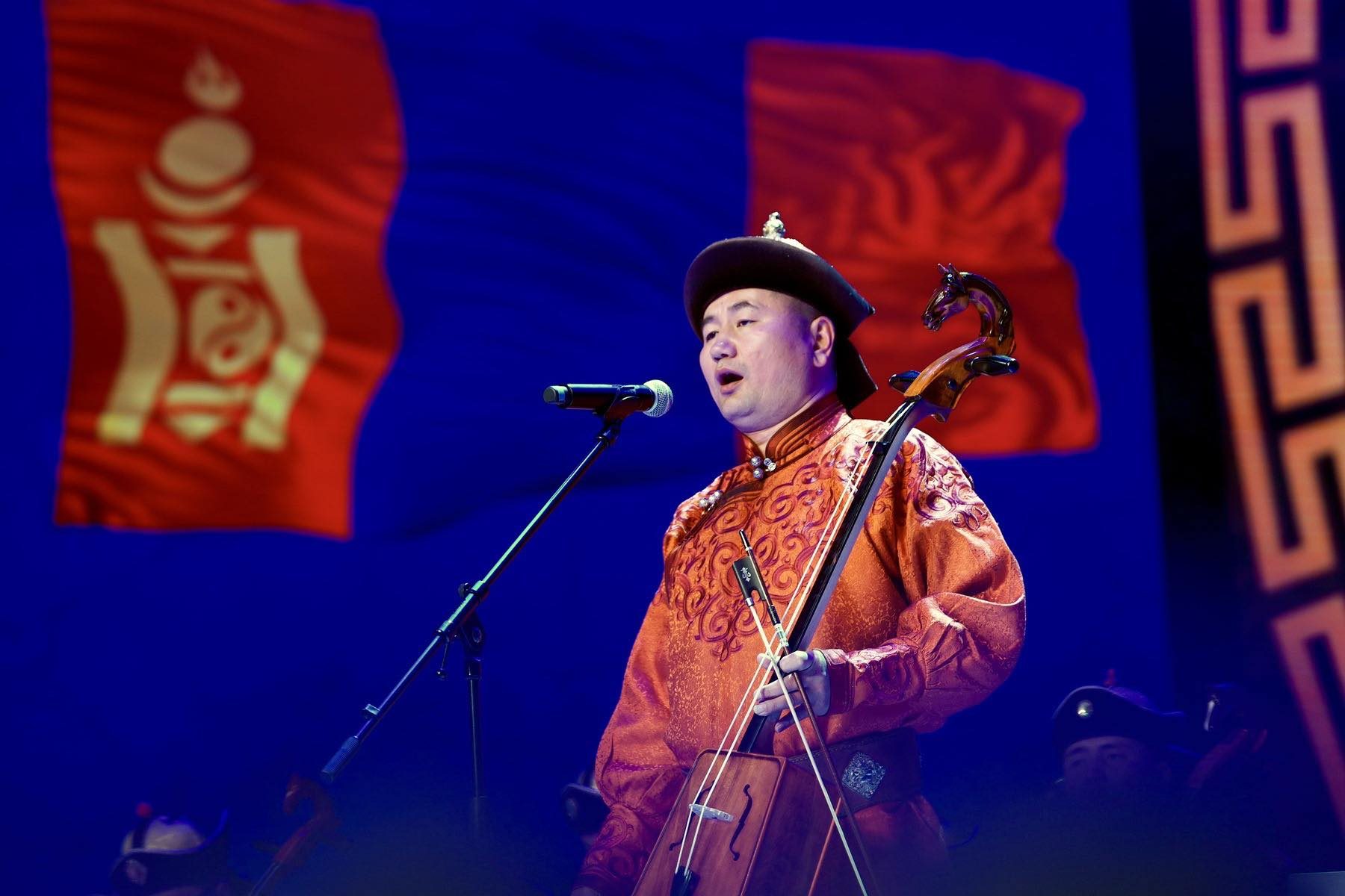 N. Ashit singing on stage with a morin khuur, in front of the Mongolian flag